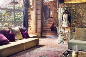 Una acogedora sala de estar con paredes de piedra, cojines de colores y un maniquí en una vitrina cerca de la escalera evoca el encantador ambiente del Hotel Castell d'Emporda en Girona. - ForTwo - Planes para parejas
