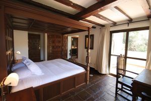 En el Hotel Castillo de Monda de Málaga, disfrute de un dormitorio rústico con una cama con dosel de madera, muebles elegantes y un impresionante techo con vigas, todo ello bañado por la luz natural que entra por un gran ventanal. - ForTwo - Planes para parejas