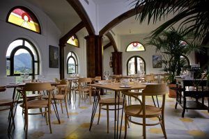 Situado en Málaga, el elegante restaurante del Hotel Castillo de Monda cuenta con sillas de madera, mesas circulares, ventanas arqueadas con vidrieras y exuberantes plantas de interior. - ForTwo - Planes para parejas