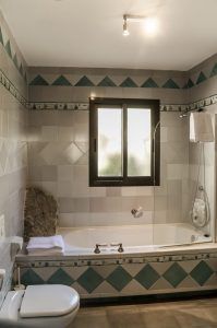 El baño, haciendo eco del encanto atemporal del Hotel Castillo de Monda (Málaga), incluye una bañera, una ventana y un inodoro adornados con azulejos cuadrados verdes y blancos. - ForTwo - Planes para parejas