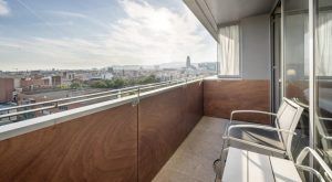 Experimente la impresionante vista del horizonte de Barcelona y las montañas distantes desde su Junior Suite: el secreto de Ilunion Hotels, con modernas barandillas y cómodas sillas. - ForTwo - Planes para parejas