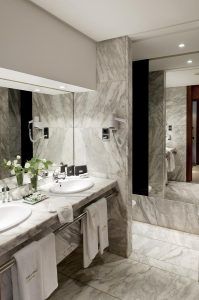 La suite presidencial del Hotel Barceló Sevilla Renacimiento cuenta con un elegante baño de mármol con lavabos dobles, espejos de pared, toallas blancas y flores frescas. - ForTwo - Planes para parejas