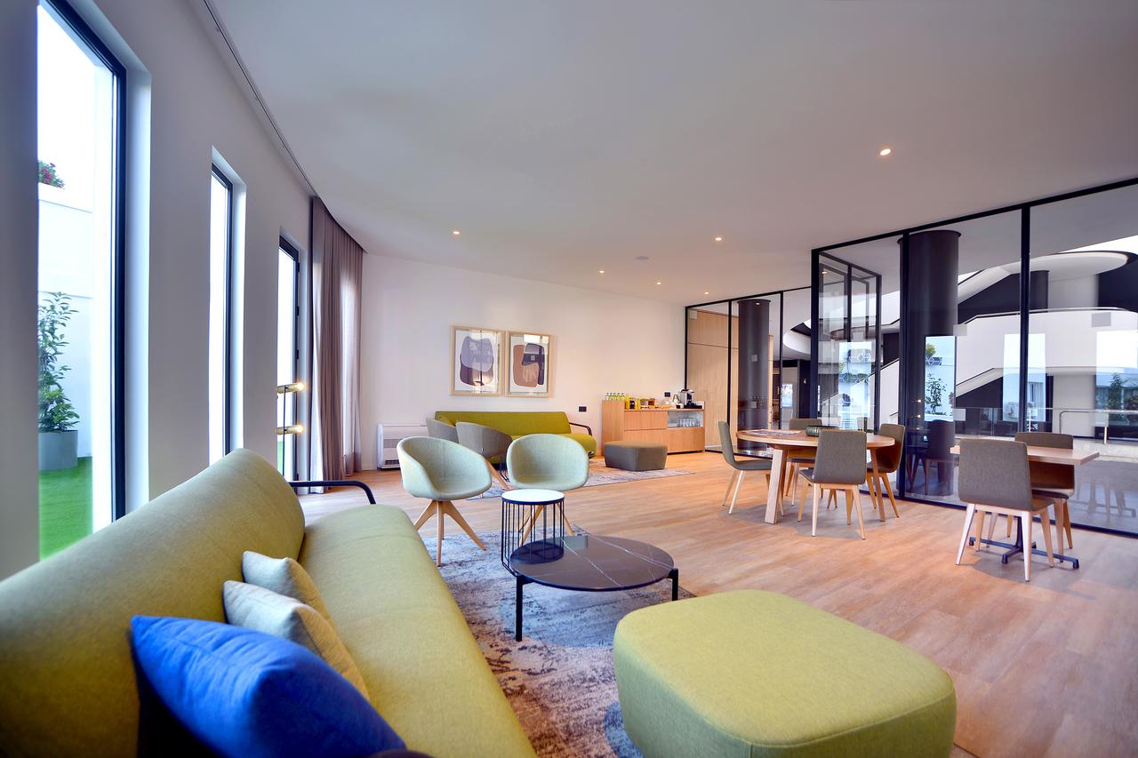 Una espaciosa sala de estar moderna que recuerda a La suite presidencial del Hotel Barceló Sevilla Renacimiento en Sevilla, con sofás verdes, mesas redondas, grandes ventanales y suelos de madera. - ForTwo - Planes para parejas