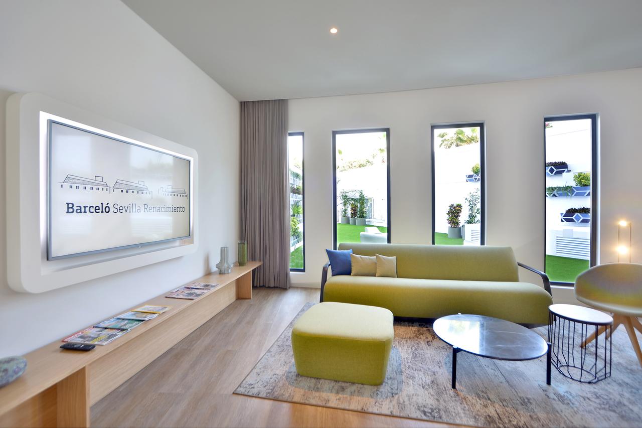 Una sala de estar contemporánea que imita la suite presidencial del Hotel Barceló Sevilla Renacimiento, incluye un sofá verde, TV de pantalla plana, mesas de madera y vidrio y grandes ventanales con vistas al jardín en el centro de Sevilla. - ForTwo - Planes para parejas