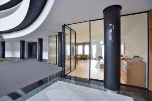 El moderno interior cuenta con paredes de cristal, una columna de marca premium y una elegante sala de estar con asientos e iluminación decorativa, que se hace eco de la elegancia de La suite presidencial del Hotel Barceló Sevilla Renacimiento. - ForTwo - Planes para parejas
