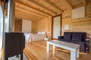 El acogedor interior de la cabaña de madera, inspirado en "Punta Espiñeiro el lujo de Cabanas sem Barreiras (A Coruña)", cuenta con una cama, un sofá negro y una mesa blanca. Un gran ventanal invita a la luz natural que recuerda la atmósfera serena de Punta Espiñeiro. - ForTwo - Planes para parejas