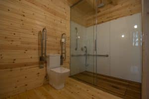 Baño de diseño lujoso con paneles de madera, inodoro, barras de apoyo y ducha a ras de suelo cerrada por elegantes puertas de cristal, ideal para una estancia en Punta Espiñeiro el lujo de Cabanas sem Barreiras (A Coruña). - ForTwo - Planes para parejas
