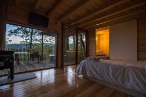 El Punta Espiñeiro el lujo de Cabanas sem Barreiras (A Coruña) ofrece acogedoras habitaciones con interiores de madera, una cama y una terraza abierta con vistas a los árboles y las colinas de Punta Espiñeiro al atardecer. - ForTwo - Planes para parejas