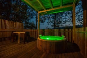 Un jacuzzi circular con agua verde brillante se encuentra en una terraza de madera bajo una encantadora pérgola, rodeado del susurro de los árboles. Ubicado en Punta Espiñeiro, el lujo de Cabanas sem Barreiras (A Coruña), este tranquilo lugar ofrece la escapada perfecta. - ForTwo - Planes para parejas