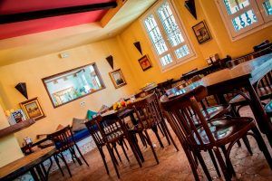 Restaurante íntimo con sillas y mesas de madera y una decoración vibrante que recuerda a las Suites románticas con jacuzzi Alcoba del Rey de Sevilla, incluyendo una pequeña ventana y arte en la pared. - ForTwo - Planes para parejas