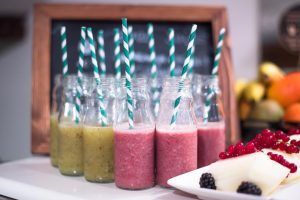 Batidos de frutas variados con pajitas rayadas en botellas se presentan elegantemente dispuestos junto a un plato de frutas y bayas en rodajas, capturando la esencia de la "Estancia de ensueño en el Hotel Petit Palace" de Bilbao. - ForTwo - Planes para parejas