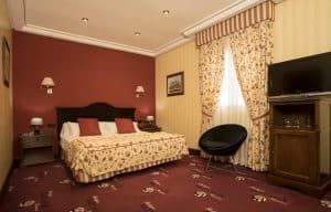 Disfrute de una acogedora estancia en la Habitación mágica en el Hotel Spa Arzuaga (Valladolid) con cama de matrimonio, cortinas estampadas, pared de acento rojo, TV de pantalla plana y un acogedor sillón junto a la ventana para momentos de relax. - ForTwo - Planes para parejas