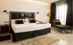 Experimente la elegante Habitación mágica del Hotel Spa Arzuaga en Valladolid, que cuenta con una gran cama con detalles oscuros, una tumbona y una bandeja de desayuno para una escapada inolvidable. - ForTwo - Planes para parejas