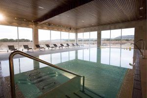 La piscina cubierta, con sus grandes ventanales que ofrecen vistas encantadoras y tumbonas bajo un techo de madera, captura la serena elegancia de la Habitación mágica en el Hotel Spa Arzuaga (Valladolid). - ForTwo - Planes para parejas