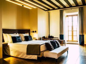 Disfrute de la experiencia Estancia en la Abadía Retuerta LeDomaine (Valladolid) en su habitación de hotel, con una cama grande, almohadas de lujo y un encantador banco sobre suelo de madera. La luz del sol, a través de elegantes cortinas, crea un ambiente cálido para una relajación total. - ForTwo - Planes para parejas