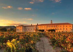 Al atardecer, la histórica Estancia en la Abadía Retuerta LeDomaine en Valladolid se rodea de viñedos con parras verdes y rojizas bajo un cielo dorado. - ForTwo - Planes para parejas