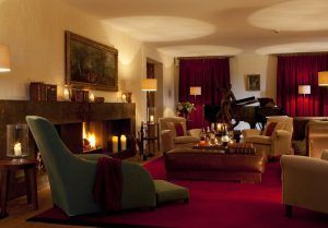Una elegante sala de estar en Estancia en la Abadía Retuerta LeDomaine (Valladolid) cuenta con una acogedora chimenea, lujosos asientos, un piano de cola, cortinas rojas y una iluminación suave. - ForTwo - Planes para parejas