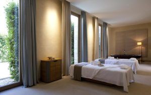 Dos mesas de masaje en una serena sala de spa en la Estancia en la Abadía Retuerta LeDomaine (Valladolid), con altos ventanales e iluminación suave, ofrecen un entorno ideal para la relajación. - ForTwo - Planes para parejas