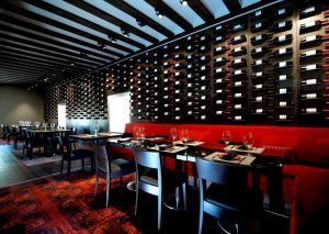 Experimente el encanto de Valladolid en el sofisticado restaurante de Estancia en la Abadía Retuerta LeDomaine, con una elegante decoración en rojo y negro, botelleros en las paredes y mesas preparadas con copas vacías. - ForTwo - Planes para parejas