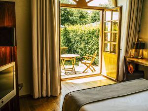 Disfrute de una acogedora habitación de hotel con una cama de lujo, televisor y acceso a un patio con sillas en medio de la exuberante vegetación de Valladolid. Disfrute de un retiro inolvidable en Estancia en la Abadía Retuerta LeDomaine. - ForTwo - Planes para parejas