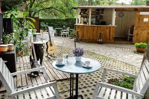 Una tranquila cafetería al aire libre cerca del Hotel Jakue cuenta con muebles de madera, guitarras y un bar rústico que refleja el encanto de la Habitación Casa del árbol Maitenea, rodeado de árboles para una escapada acogedora. - ForTwo - Planes para parejas