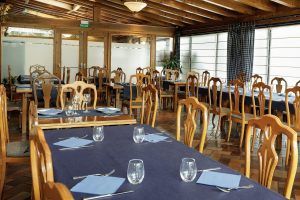 Un espacio vacío para comer en el Hotel Maitenea (Navarra), con sillas de madera y mesas con manteles azul marino elegantemente dispuestas con vasos y servilletas. - ForTwo - Planes para parejas