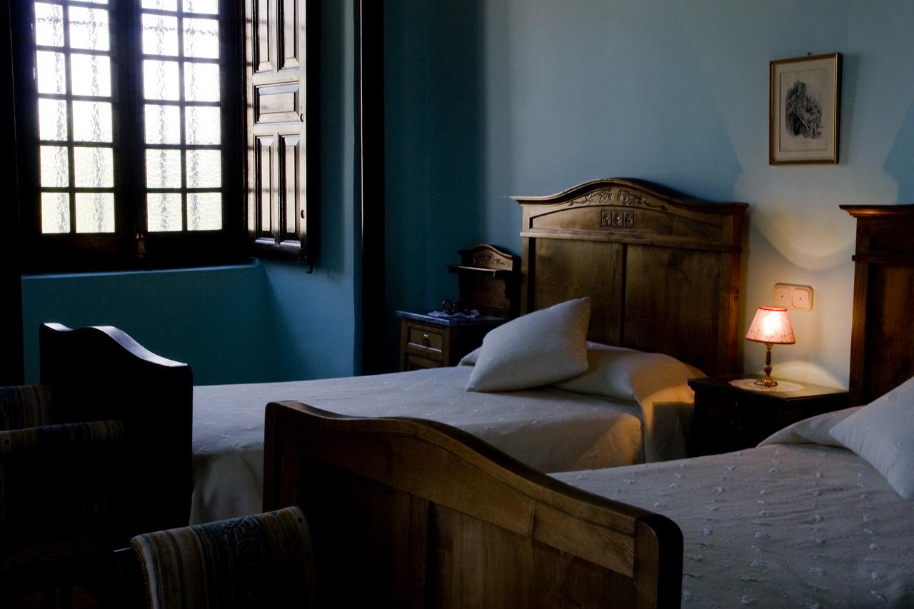 Experimente la comodidad en La Posada de Pradorey, Burgos, con dos camas de madera, una suave iluminación en la lámpara de noche y una ventana enmarcada por encantadoras contraventanas de madera. - ForTwo - Planes para parejas