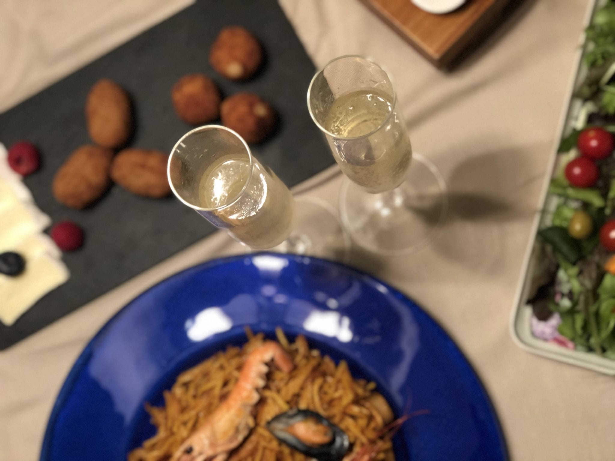 La mesa está adornada con dos copas de champán, un plato de pasta con marisco y una variedad de aperitivos, creando una deliciosa experiencia que recuerda al Día romántico de vino y gastronomía entre viñedos (Barcelona). - ForTwo - Planes para parejas