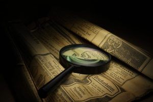 Una lupa se cierne sobre viejos periódicos alemanes amarillentos. Un artículo menciona, curiosamente, "Deutsch Arbeiten". Parece como Resuelve el Misterio del Hotel Escape Room (Zafra), donde cada palabra revela capas de misterio esperando ser descubiertas. - ForTwo - Planes para parejas
