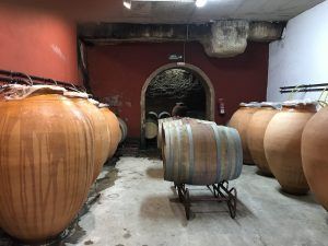 Ánforas de barro y barriles de madera en una bodega poco iluminada capturan la esencia del Día romántico del vino y la gastronomía entre viñedos (Barcelona), con paredes rojas y blancas que reflejan el rico tapiz de vinos y viñedos. - ForTwo - Planes para parejas