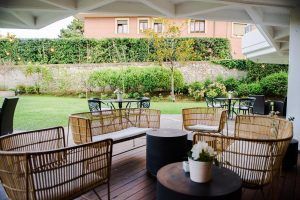 Disfrute de una escapada romántica en el acogedor patio del Gran Hotel Victoria en Santander, con sillas de mimbre, mesas, césped verde, elegantes setos y cerramiento de pared de piedra, perfecto para su "Escapada romántica al Gran Hotel Victoria con botella de cava". - ForTwo - Planes para parejas