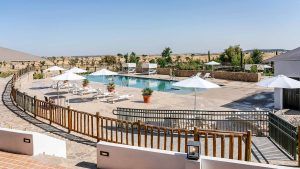 Disfrute de una lujosa piscina al aire libre en el Hospes Palacio de Arenales de Cáceres, con tumbonas y sombrillas blancas, rodeada por una valla de madera y con serenas vistas al campo que se integran a la perfección con la naturaleza. Ideal para un fin de semana de spa rejuvenecedor. - ForTwo - Planes para parejas