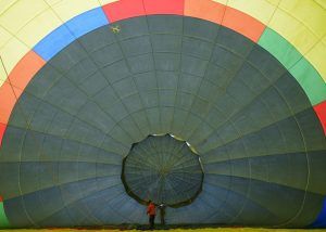 Vista interior de un colorido globo aerostático siendo inflado, con dos personas cerca del centro, listas para embarcarse en un impresionante Vuelo en globo con Barcelona Balloon Flights (Barcelona). - ForTwo - Planes para parejas