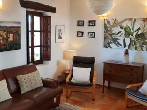 Enclavados en el corazón de las Alpujarras, los Apartamentos con cocina en las Alpujarras Cortijo Opazo (Granada) cuentan con un acogedor salón con un sofá marrón, un sillón y un arcón de madera. Obras de arte adornan las paredes mientras la luz natural inunda este acogedor oasis. - ForTwo - Planes para parejas