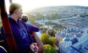 En un globo aerostático, dos personas disfrutan del Vuelo en globo con Eolofly en Aranjuez, maravillándose con la vista del amanecer de los exuberantes árboles, jardines y edificios de la ciudad. - ForTwo - Planes para parejas