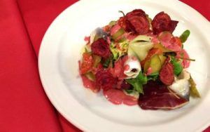 Una colorida ensalada de remolacha con verduras y finas lonchas de pescado se presenta elegantemente en un plato blanco sobre un mantel rojo, que recuerda al vibrante Menú ruso para dos en el restaurante Noches de Moscú (Madrid). - ForTwo - Planes para parejas