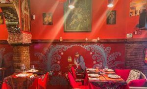 El Restaurante Noches de Moscú en Madrid ofrece un ambiente vibrante con paredes rojas y decoración elaborada. Su Menú ruso para dos transporta a los comensales al corazón de Rusia, deleitándolos con su autenticidad, mientras que las mesas elegantemente dispuestas con platos y copas de vino realzan la experiencia. - ForTwo - Planes para parejas