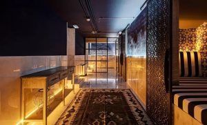 Una habitación poco iluminada con paredes estampadas, iluminación inferior brillante y una zona de estar a rayas ofrece una escapada relajante que recuerda al Circuito de spa con masaje para dos personas del Hotel Pestana Plaza Mayor de Madrid. - ForTwo - Planes para parejas