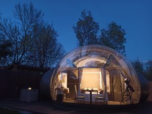 Descubre la encantadora Escapada romántica en hotel burbuja con Gredos Estelar en Ávila, que cuenta con una cúpula iluminada enclavada entre árboles, completa con una mesa y un telescopio para observar las estrellas bajo el cielo nocturno. - ForTwo - Planes para parejas