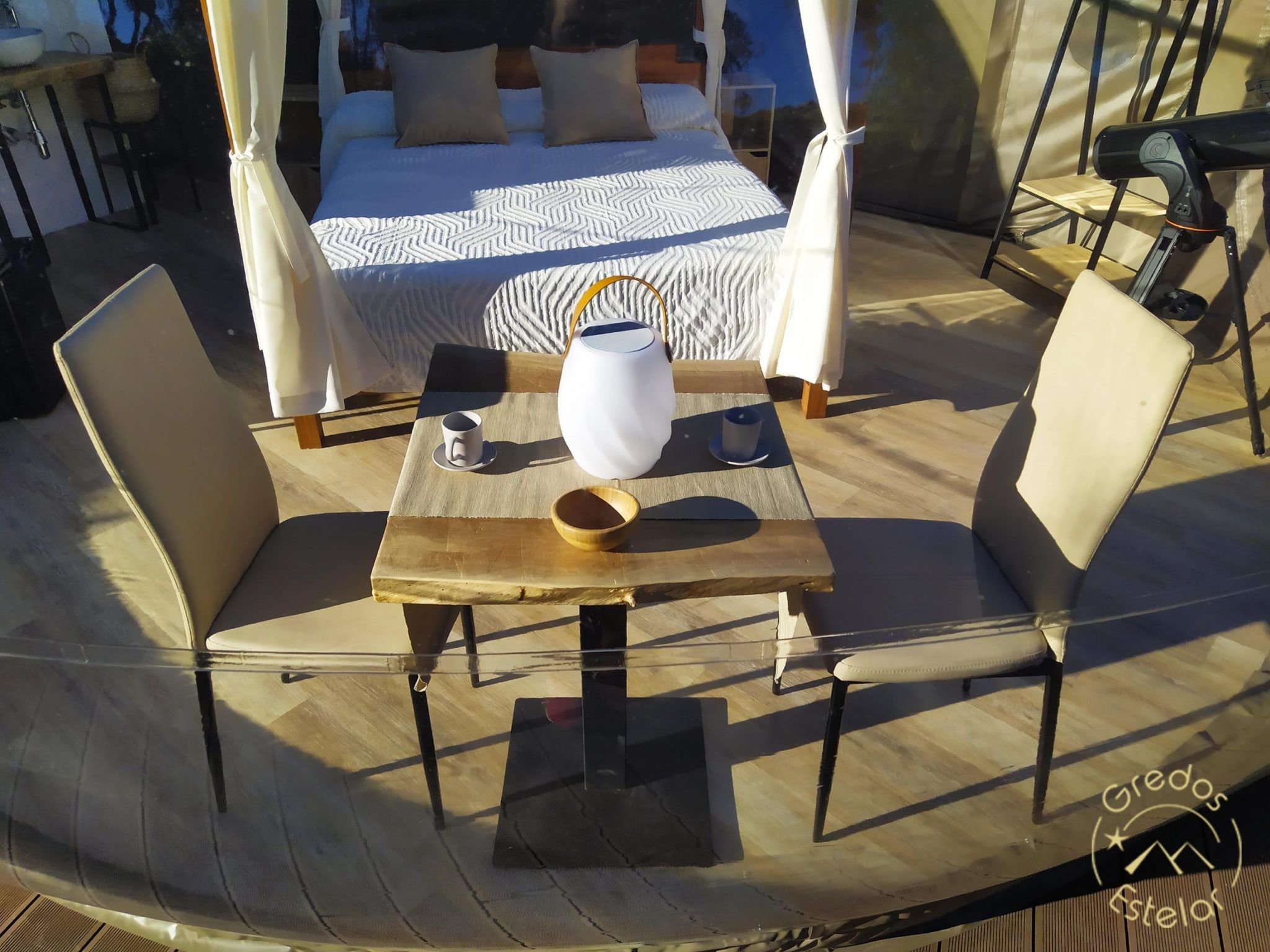 Relájese en el acogedor interior de una cabaña en Escapada romántica en el hotel Burbuja con Gredos Estelar (Ávila). Disfrute de una mesa de comedor y sillas frente a la cama, con una encantadora tetera y tazas, para un refugio idílico que captura la serenidad de Gredos Estelar. - ForTwo - Planes para parejas