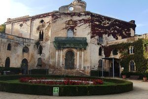 Una mansión cubierta de hiedra, que recuerda la elegancia atemporal de Barcelona, presenta un parterre circular y un contenedor de reciclaje en primer plano durante el Free tour por el Laberinto de Horta (Barcelona). - ForTwo - Planes para parejas