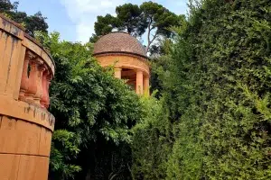En medio de una exuberante vegetación, un cenador de ladrillo con techo abovedado se alza majestuoso bajo el cielo despejado de Barcelona, evocando la serena belleza del Laberinto de Horta. Únete al "Tour gratuito por el Laberinto de Horta (Barcelona)" para explorar este pintoresco entorno. - ForTwo - Planes para parejas