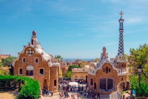Bajo el cielo azul, una multitud vibrante admira los coloridos edificios del Parque Güell, adornados con mosaicos. Esta icónica atracción barcelonesa captura el espíritu artístico de la ciudad y ofrece a quienes participan en un "Tour gratuito por el Parque Güell (Barcelona)" un entorno pintoresco. - ForTwo - Planes para parejas