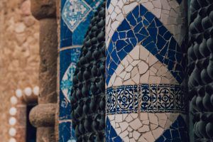 Un pilar de mosaico detallado que presenta patrones geométricos azules y blancos en un entorno de piedra texturizada, que se hace eco del arte vibrante del Free Tour por el Park Güell de Barcelona. - ForTwo - Planes para parejas