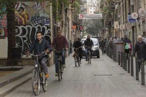 Las bicicletas recorren una calle adornada con grafitis en Barcelona, con peatones y un coche sumándose a la animada escena, como si la propia ciudad ofreciera un "Tour gratuito por Barcelona" a través de su colorido lienzo urbano. - ForTwo - Planes para parejas