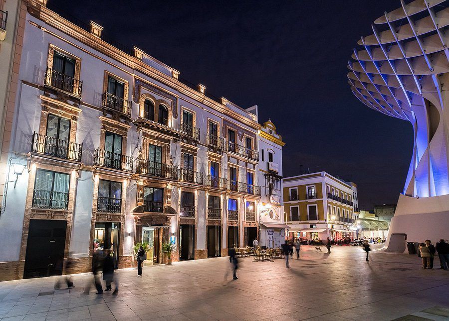 En medio de la encantadora escena nocturna de Sevilla, los edificios históricos brillan cálidamente junto a una sorprendente estructura moderna, mientras la gente pasea y cena al aire libre cerca del elegante Hotel Casa de Indias by Intur con spa y desayuno. - ForTwo - Planes para parejas