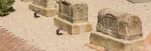Descubra cuatro antiguas tumbas de piedra con inscripciones a lo largo de un sendero de grava en el Free Tour por la Barcelona Romana. Cada tumba cuenta con una pequeña etiqueta que ofrece información sobre la rica historia de la ciudad a través de esta fascinante experiencia. - ForTwo - Planes para parejas