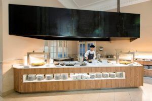En el lujoso ambiente del Balneario Caldes de Montbui, un chef prepara con arte el desayuno, presentado de forma cuidada en elegantes estaciones de servicio. - ForTwo - Planes para parejas
