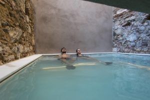 La sesión es como un tranquilo spa: dos personas se relajan en una piscina cubierta con paredes de piedra y hormigón, gracias a la Escapada con desayuno y spa en Balneario Caldes de Montbui, Barcelona. - ForTwo - Planes para parejas