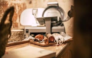 La rústica Comida o cena de productos locales en l'Espai Quera (Barcelona) presenta charcutería con salchichas en rodajas y queso sobre una tabla de madera, resaltando sabores ricos perfectos para una comida acogedora. - ForTwo - Planes para parejas